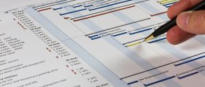 Detailed Gantt Chart showing Tasks, Resources and Notes. Includes a pen being held by a man on the right.