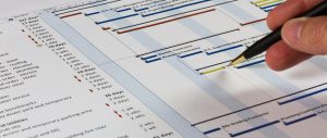 Detailed Gantt Chart showing Tasks, Resources and Notes. Includes a pen being held by a man on the right.